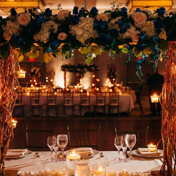 Elegant dining table with a large floral and candle centerpiece in a warmly lit event hall.