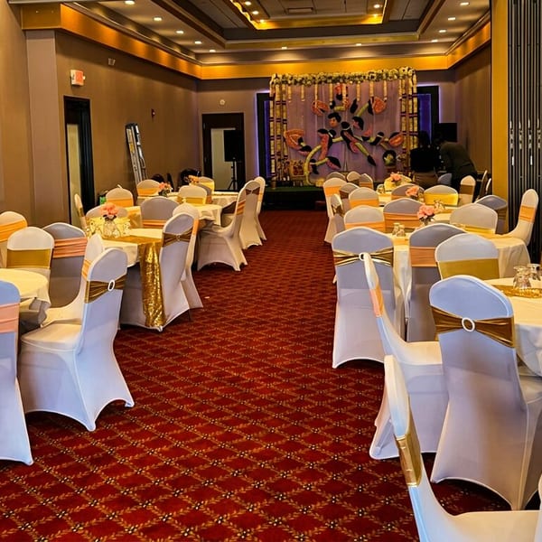 Decorated banquet hall with round tables, white chairs, orange sashes, and a stage.