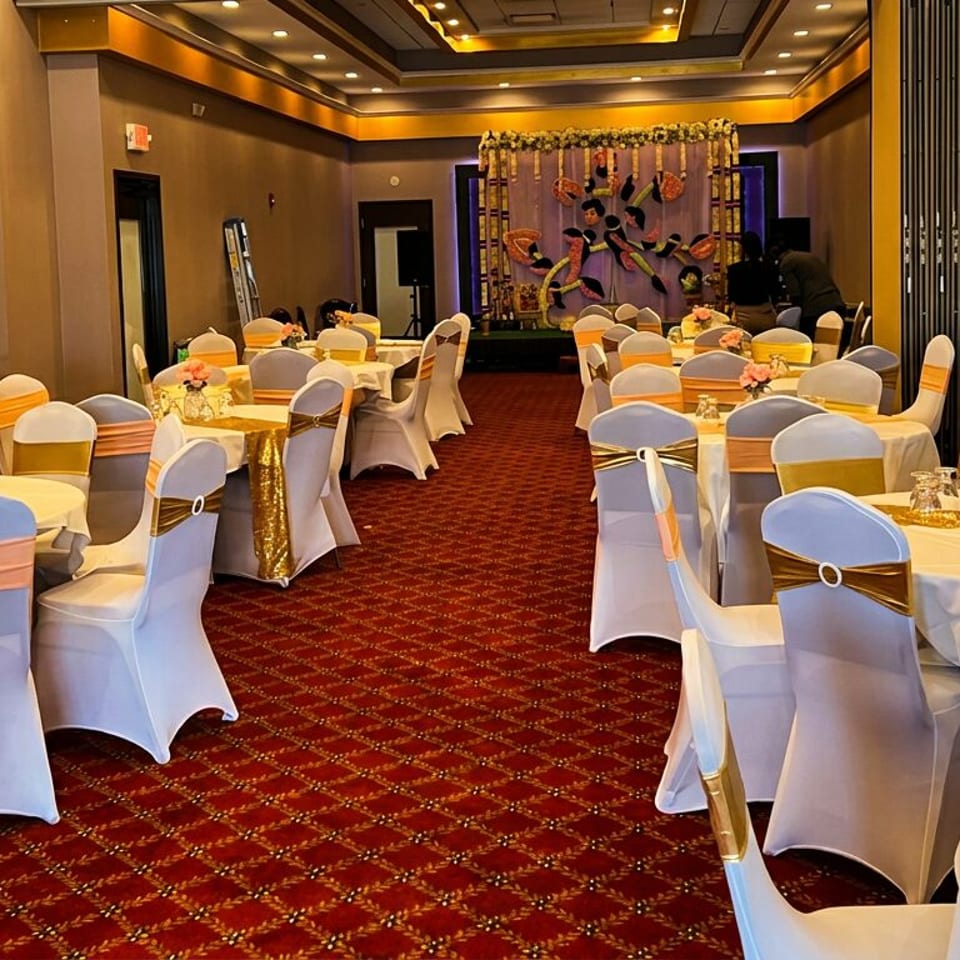 Decorated banquet hall with round tables, white chairs, orange sashes, and a stage.
