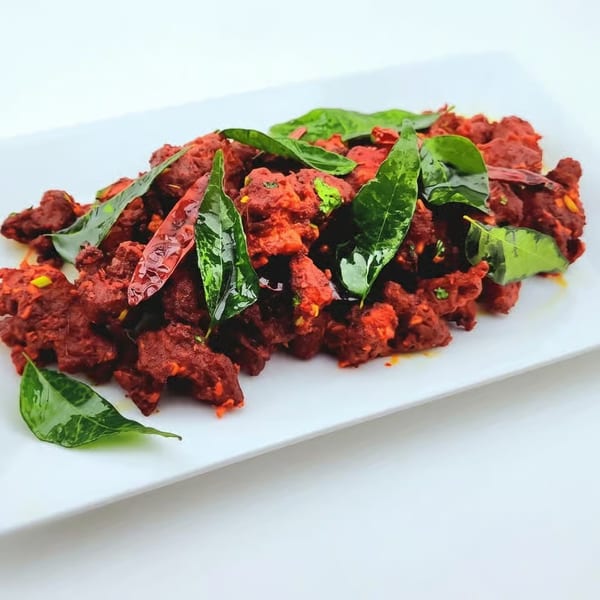 Spicy red fried chicken pieces garnished with fresh curry leaves and dried red chilies.