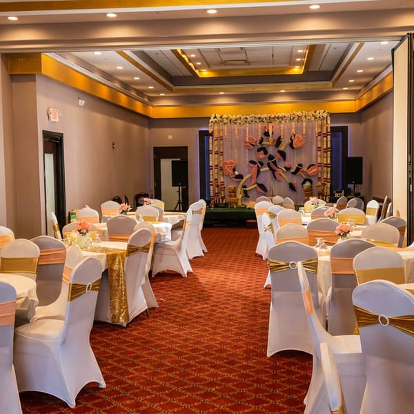 Banquet hall with white and gold decorated tables and chairs, and an ornate stage.
